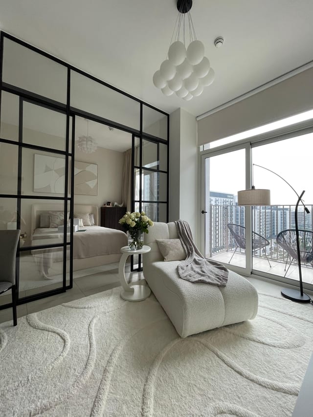 Living room of the Dubai Hills apartment by Anna Arsentyeva: glazed steel-framed partition to the bedroom, boucle chaise, arc floor lamp, balcony over Dubai Hills